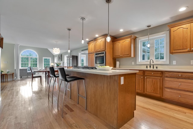 kitchen featuring stainless steel appliances, a kitchen island, light wood-style floors, decorative light fixtures, and light countertops