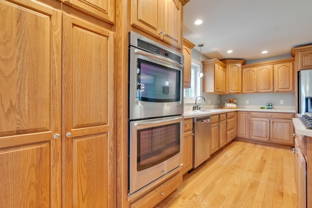 kitchen featuring stainless steel appliances, a sink, light countertops, light wood finished floors, and recessed lighting