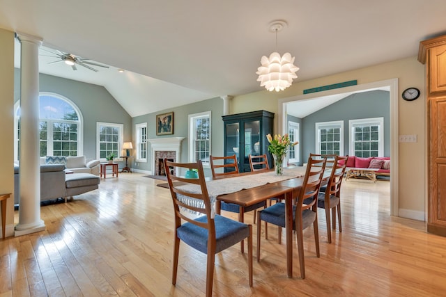 dining space with decorative columns, vaulted ceiling, light wood-style flooring, a fireplace, and a ceiling fan