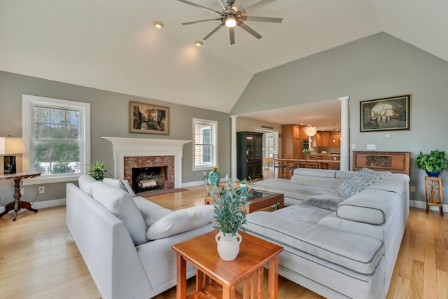 living area featuring ceiling fan, vaulted ceiling, baseboards, light wood finished floors, and a fireplace
