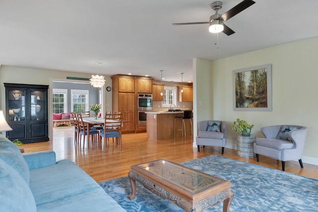 living room with a ceiling fan, light wood-style flooring, a chandelier, and baseboards