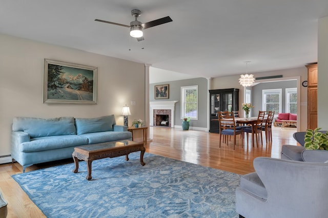 living room with light wood-type flooring, ceiling fan, a fireplace with flush hearth, and a chandelier