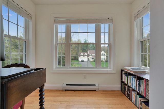 living area with baseboard heating, healthy amount of natural light, baseboards, and hardwood / wood-style flooring