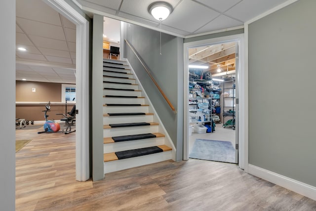 stairway with wood finished floors, a drop ceiling, and baseboards
