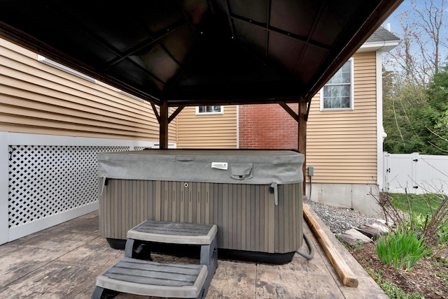 view of patio featuring a hot tub, a gazebo, and fence