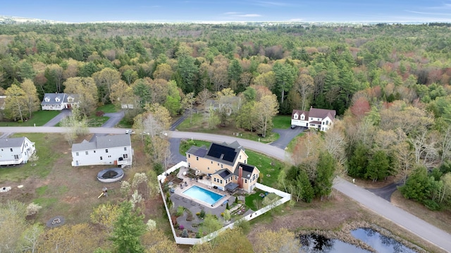 drone / aerial view of a heavily wooded area, a pool, and a large body of water