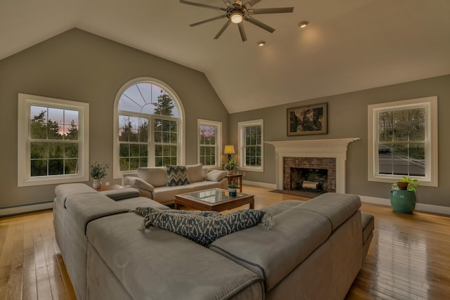 living area with ceiling fan, vaulted ceiling, baseboard heating, light wood finished floors, and a fireplace with flush hearth