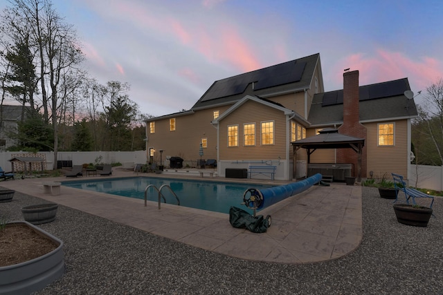 back of property at dusk featuring a jacuzzi, a gazebo, a patio area, roof mounted solar panels, and a fenced backyard