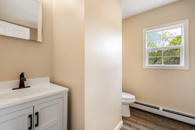 half bathroom with a baseboard radiator, vanity, wood finished floors, and toilet