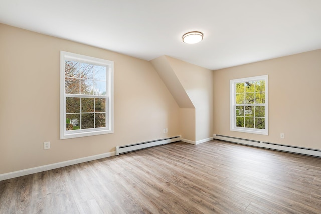 additional living space with baseboard heating, wood finished floors, and healthy amount of natural light
