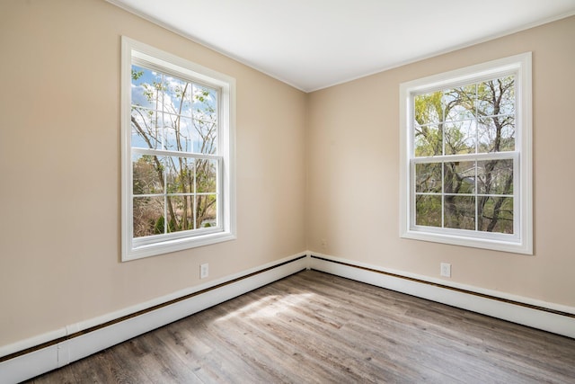 empty room featuring wood finished floors, plenty of natural light, and a baseboard heating unit