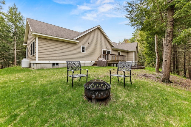 back of house featuring an outdoor fire pit, a deck, roof with shingles, and a yard