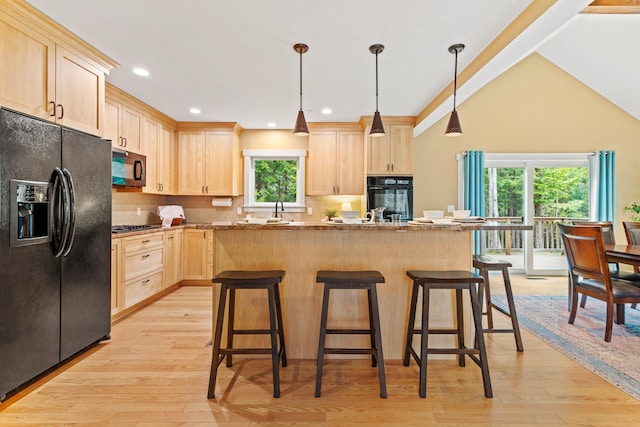 kitchen featuring light brown cabinetry, a kitchen bar, a kitchen island, backsplash, and black appliances