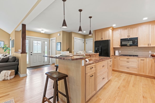 kitchen with black appliances, light wood finished floors, light brown cabinets, and a breakfast bar area