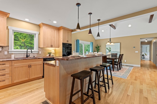 kitchen with a sink, light wood finished floors, decorative backsplash, and light brown cabinetry
