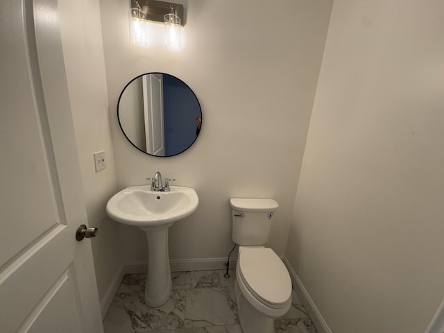 half bath featuring marble look tile flooring, toilet, baseboards, and a sink