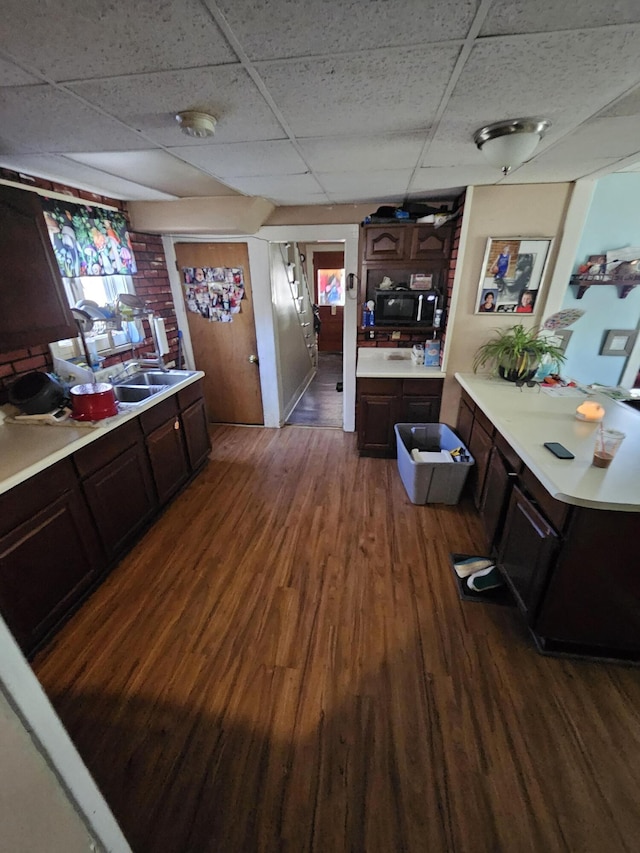 kitchen featuring black microwave, light countertops, dark wood-style floors, a paneled ceiling, and dark brown cabinets