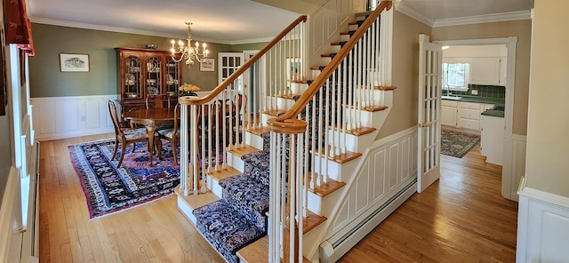 196 Eaton Ridge Dr, Holden, ME 04429 - staircase featuring a baseboard radiator, wood finished floors, a chandelier, ornamental molding, and wainscoting
