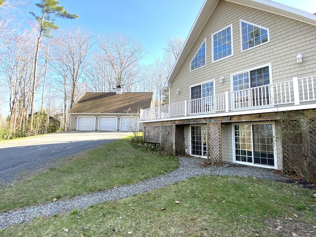 back of property featuring a yard, an outdoor structure, a deck, and a garage
