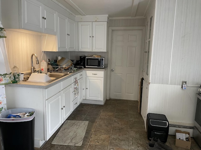 kitchen with stainless steel microwave, a sink, white cabinetry, dark stone finish flooring, and ornamental molding