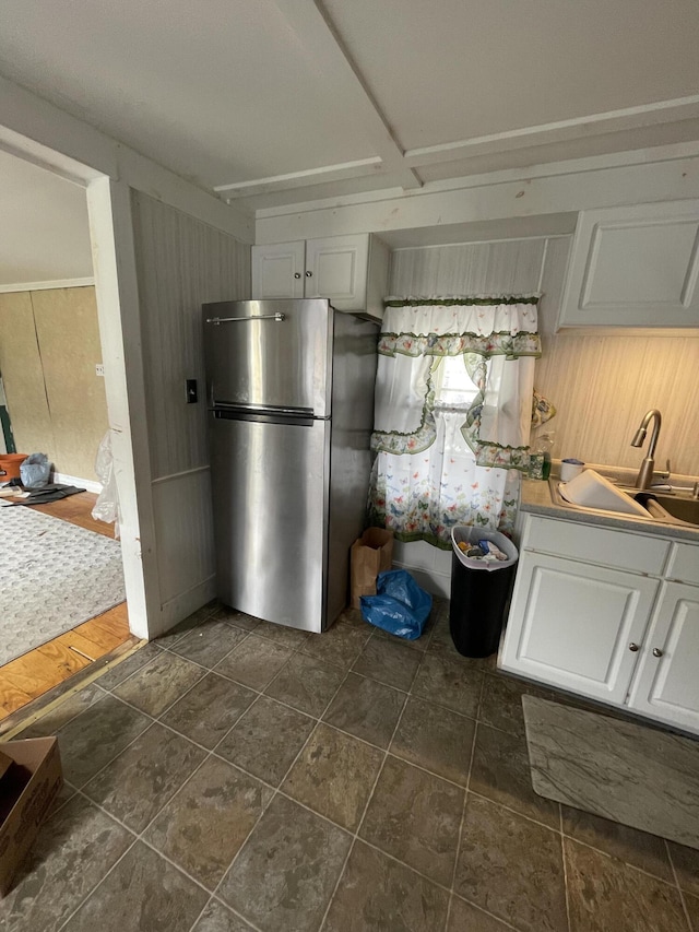 kitchen featuring freestanding refrigerator, a sink, white cabinets, and wooden walls