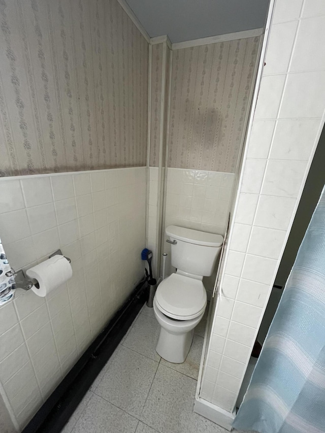 bathroom featuring wallpapered walls, wainscoting, toilet, tile patterned floors, and tile walls