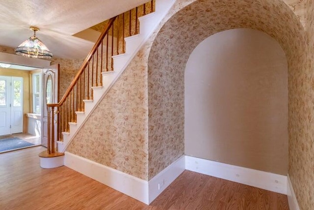 753 Sebec Village Rd, Sebec, ME 04481 - foyer entrance featuring arched walkways, wood finished floors, wallpapered walls, stairs, and baseboards