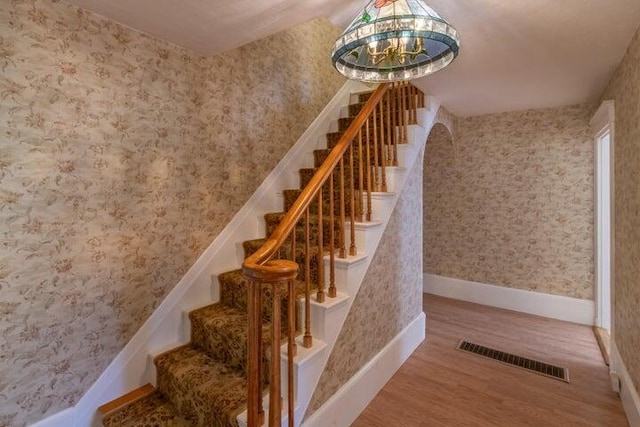 753 Sebec Village Rd, Sebec, ME 04481 - stairway featuring wood finished floors, baseboards, wallpapered walls, and a chandelier