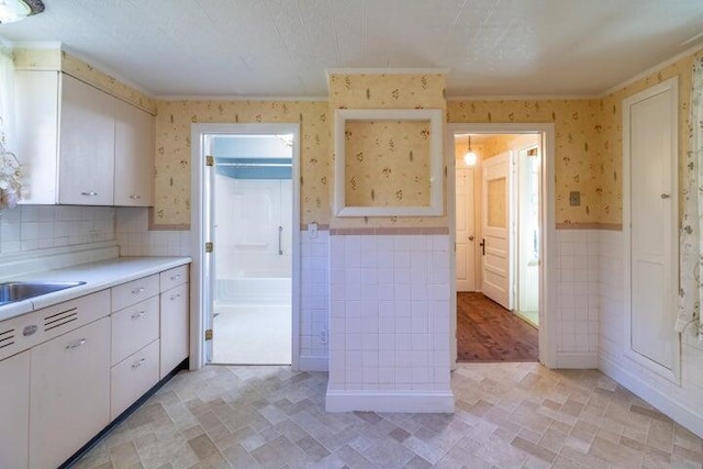753 Sebec Village Rd, Sebec, ME 04481 - kitchen featuring wallpapered walls, wainscoting, ornamental molding, white cabinetry, and light countertops