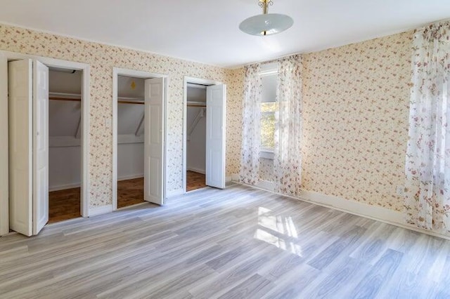 753 Sebec Village Rd, Sebec, ME 04481 - unfurnished bedroom with multiple closets, wallpapered walls, wood finished floors, and baseboards