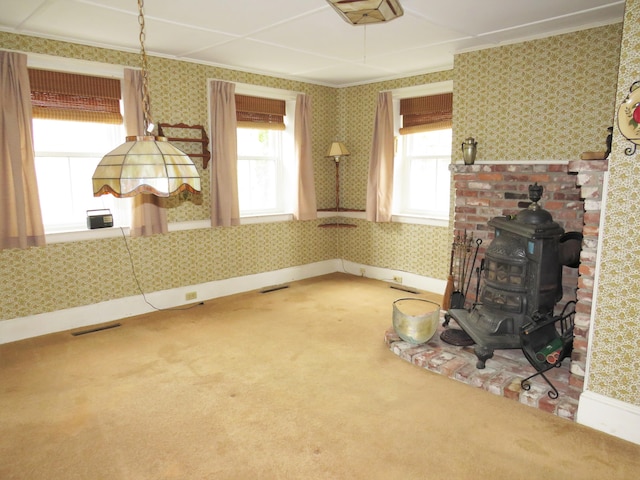 unfurnished living room with a wood stove, plenty of natural light, carpet flooring, and wallpapered walls