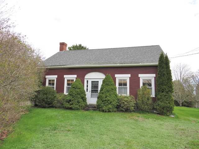 view of front of house with roof with shingles, a chimney, and a front yard