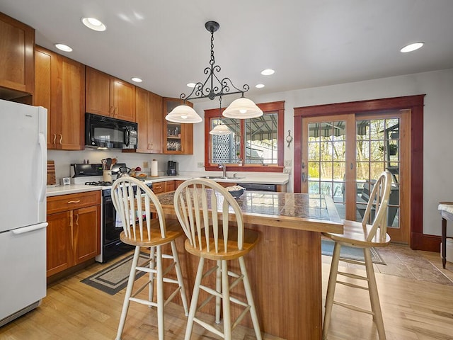 kitchen featuring black microwave, freestanding refrigerator, range with gas cooktop, brown cabinets, and a breakfast bar