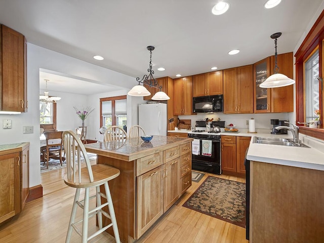 kitchen featuring gas stove, black microwave, a sink, freestanding refrigerator, and a breakfast bar area