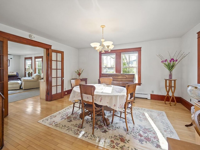dining room featuring a chandelier, light wood finished floors, baseboard heating, and baseboards