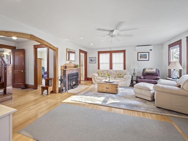 living area with light wood-style flooring, a ceiling fan, arched walkways, a wall mounted AC, and stairway