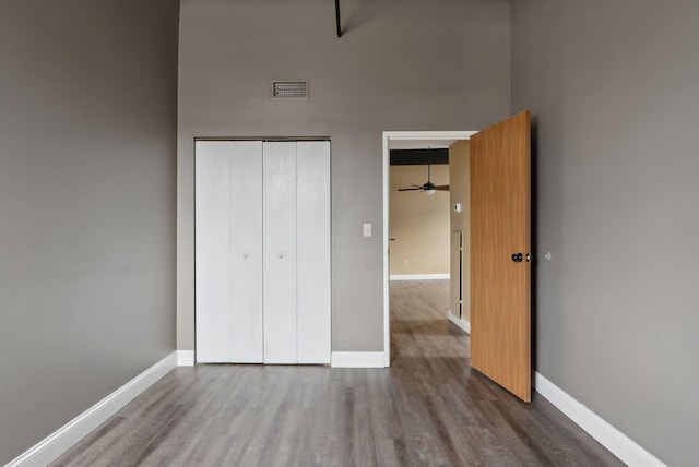 unfurnished bedroom with wood finished floors, baseboards, a closet, and a towering ceiling