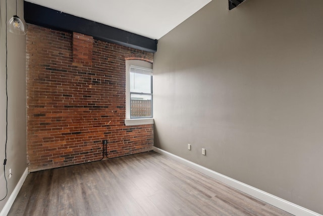 spare room featuring wood finished floors, baseboards, and brick wall