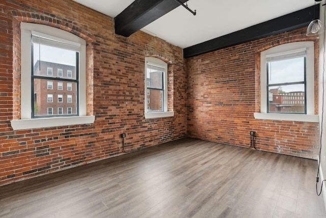 unfurnished room featuring beamed ceiling, healthy amount of natural light, wood finished floors, and brick wall