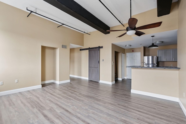 unfurnished living room featuring a barn door, high vaulted ceiling, a ceiling fan, wood finished floors, and baseboards