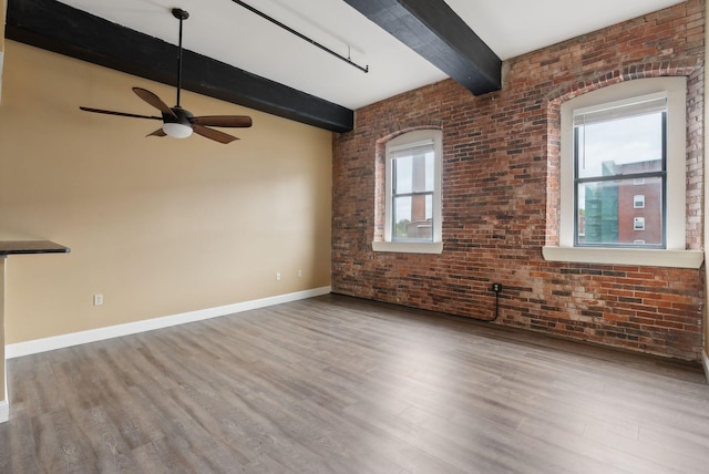 unfurnished room with beamed ceiling, ceiling fan, wood finished floors, baseboards, and brick wall