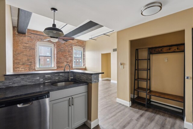 kitchen with stainless steel dishwasher, a sink, a ceiling fan, wood finished floors, and brick wall
