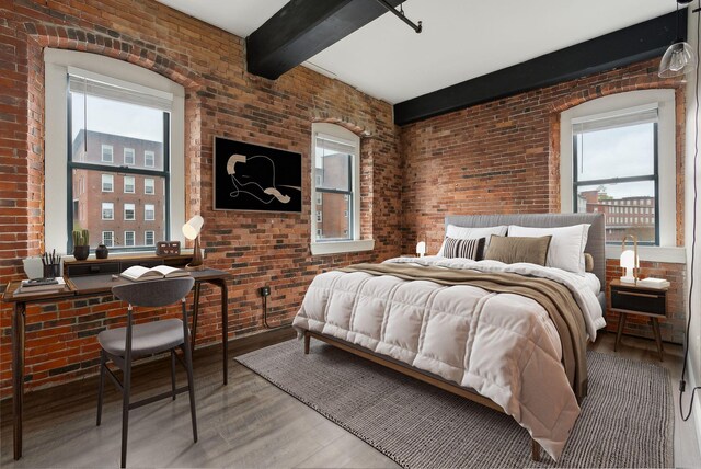 bedroom with brick wall, beam ceiling, and wood finished floors