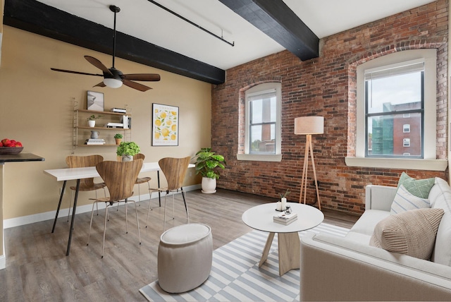 sitting room with beamed ceiling, wood finished floors, baseboards, brick wall, and ceiling fan