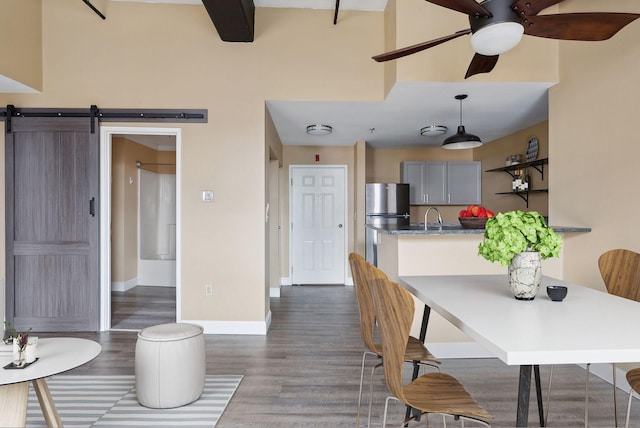 dining area featuring ceiling fan, dark wood-type flooring, baseboards, and a barn door