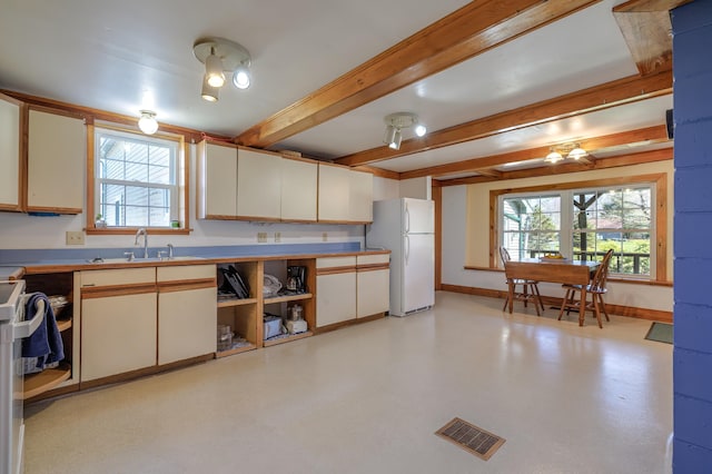 kitchen with freestanding refrigerator, a healthy amount of sunlight, visible vents, a sink, and beamed ceiling