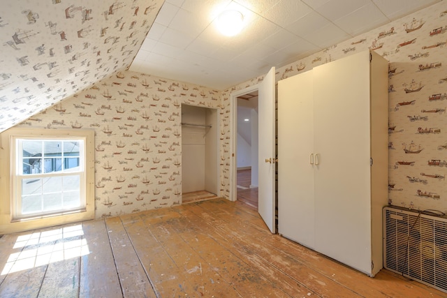 additional living space featuring vaulted ceiling, light wood finished floors, wallpapered walls, and visible vents