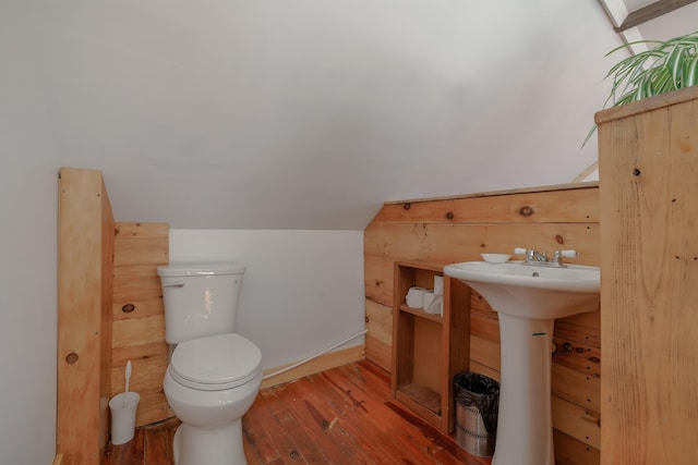 bathroom featuring toilet, wood finished floors, a sink, wooden walls, and lofted ceiling