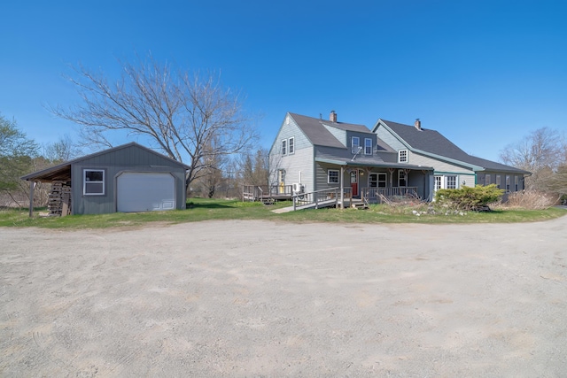 exterior space featuring a chimney, dirt driveway, an outdoor structure, covered porch, and a garage