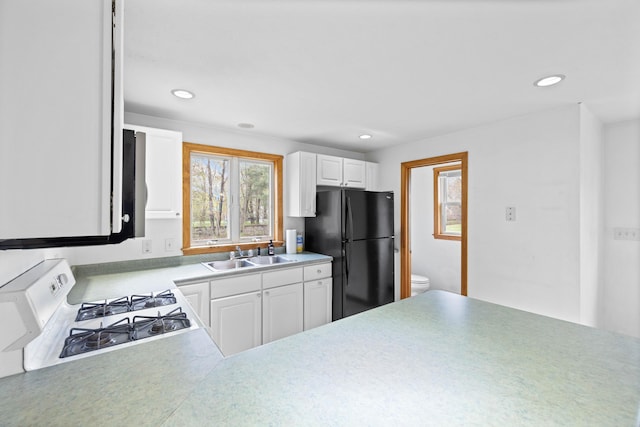kitchen with freestanding refrigerator, a sink, white gas range, white cabinetry, and recessed lighting